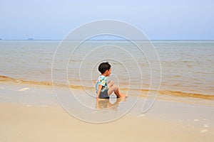 Asian little boy sitting on tropical sand beach with looking at sea
