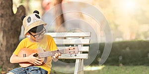 An Asian little boy wearing glasses is happily playing the ukulele. Asian little child is trying to play the ukulele with a fully