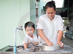 Asian little child boy helping grandmother wash pot with happy smiling face.