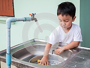 Asian little child boy helping to wash pot with happy face in relaxing family time.