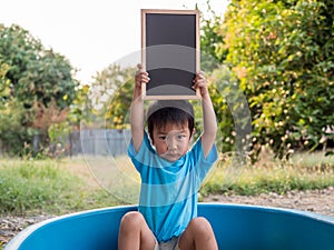 Asian little child boy holding empty blank black board on head with cute serious face