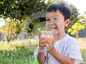 Asian little child boy holding glass of orange juice with smiling happy face