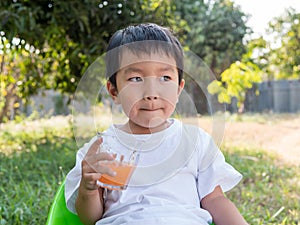 Asian little child boy holding glass of orange juice with smiling