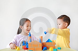 Asian little child girl and baby boy playing a colorful wood block toy on table over white background. Sister and her brother