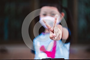 Asian little child girl closeup raise two V shape finger wear a mask to safety Coronavirus to support in the fight against disease