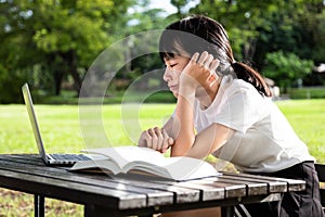 Asian little child girl feeling boring while cramming,studying online,female student with laptop computer and a book on table,