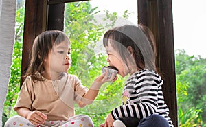 Asian little child girl and her sister are eating banana cupcake in the room deliciously