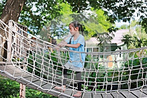 Asian little child girl playing on suspension wooden bridge. Kid walking on rope bridge Equipment at park playground