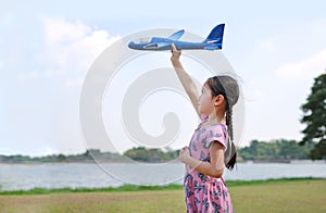Asian little child girl raise up a blue toy airplane flying on air in the nature garden. Side view