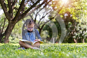 Asian little child girl reading a book in the garden