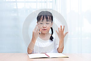 Asian little Chinese Girl doing mathematics by counting fingers photo