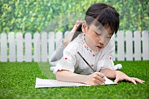 Asian Little Chinese girl kneeling on the grass and doing homework