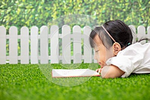 Asian Little Chinese girl kneeling on the grass and reading book