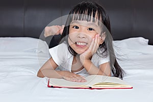 Asian little Chinese girl reading a book on bed