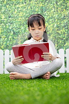 Asian Little Chinese girl sitting on the grass and reading book