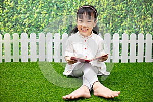 Asian Little Chinese girl sitting on the grass and reading book