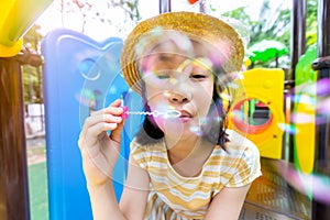 Asian little girl blowing bubbles on a playground outdoor and looking at camera,happy cute child is playing with soap bubbles in