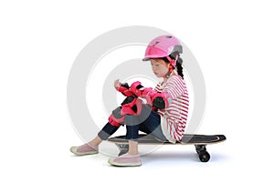 Asian little girl child skateboarder sitting on skateboard with wearing safety and protective equipment isolated on white