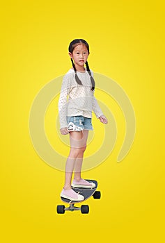 Asian little girl child skating on a skateboard isolated on yellow background. Kid riding on skateboard. Image with Clipping path