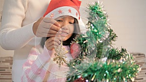 Asian little girl decorating a Christmas tree and praying for best thingHappy Asian little girl decorating a Christmas tree with h