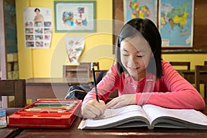 Asian little girl enjoy learning in classroom,portrait of a smiling child student studying holding pencil writing on book,sitting