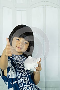 Asian little girl hand holding white piggy bank, learn to saving for the future concept