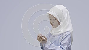 An Asian little girl in a hijab fervently prays with her arms open