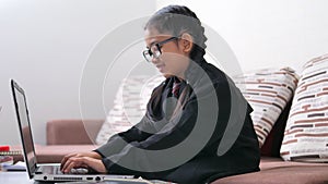 Asian little girl imagines herself as a businesswoman. The kid typing the laptop and sitting on the sofa