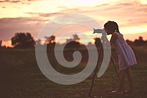 Asian little girl photographer taking picture silhouette sunset sky by digital camera on tripod standing with happy