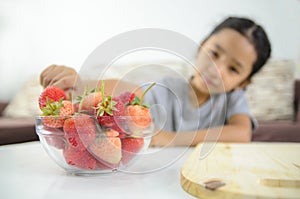 Asian little girl picking straberry in glass bowl