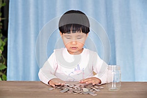 Asian little girl playing with dollar coins in glass bottle