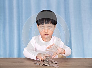Asian little girl playing with dollar coins in glass bottle