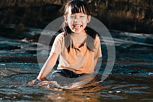 Asian little girl playing in the forest stream. Active recreation with children on river in summer