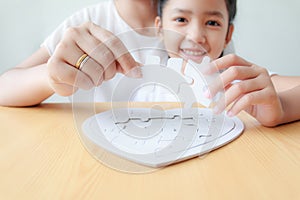 Asian little girl playing jigsaw puzzle with her mother for family concept shallow depth of field select focus on hands