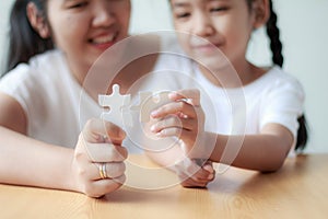 Asian little girl playing jigsaw puzzle with her mother for family concept shallow depth of field select focus on hands