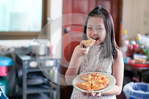 Asian little girl preparing and eating homemade pizza in the home kitchen with smile and happy