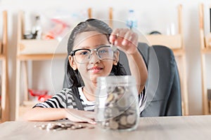 Asian little girl in putting coin in to glass jar for saving mon