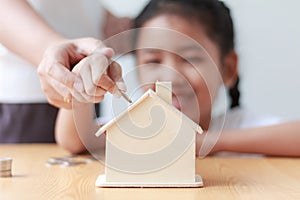 Asian little girl putting coin to house piggy bank shallow depth