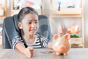 Asian little girl in putting coin in to piggy bank shallow depth of field select focus at the face