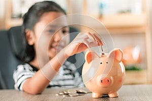 Asian little girl in putting coin in to piggy bank shallow depth of field select focus at the pig