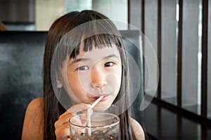 Asian Little Girl Sipping on a Straw from a Glass of Iced Beverage.