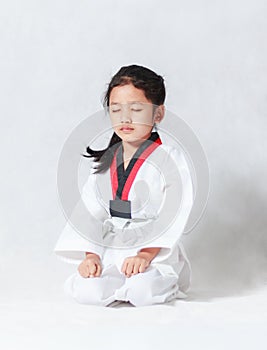 Asian little girl is sitting for concentration in taekwondo uniform on white background