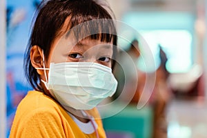 Asian little girl sitting in a hospital and wear  medical mask with sad eyes and hope . Coronavirus Covid-19 concept