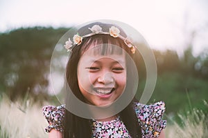 Asian little girl smiling in flower wreath in meadow field