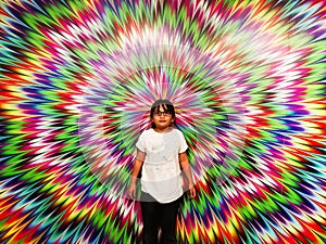 Asian little girl is standing against the optical illusion wall with circles that create the effect of moving