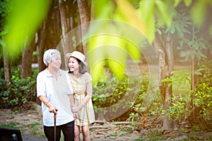 Asian little girl supporting senior woman with walking stick,happy smiling grandmother and granddaughter in the park,elderly