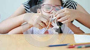 Asian little girl in Thai kindergarten student uniform and her mother using scissor to cut the white paper making family shape fat