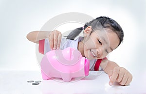 Asian little girl in Thai student uniform putting coins to piggy