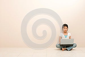 Asian little girl using a laptop and looking at camera against pink background