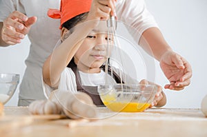 Asian little girl using stainless steel whisk to mix the egg for